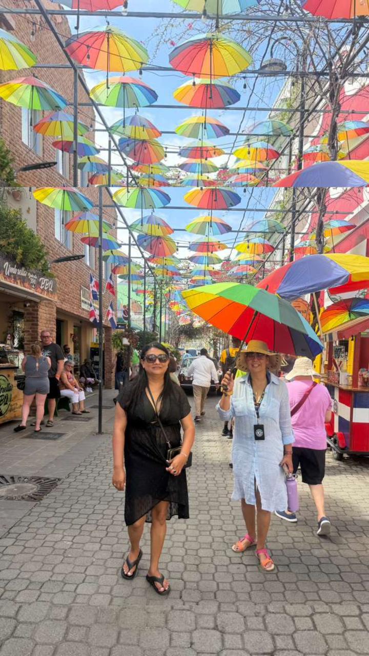 Dos amigas caminando bajo una calle techada con paraguas de colores