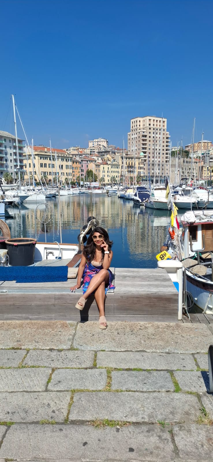 Viajera sentada junto a un puerto con veleros y edificios al fondo