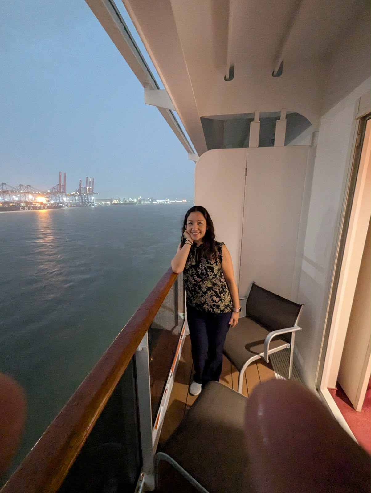 Itzel sonriendo en el balcón de su camarote durante un crucero, con el mar y el puerto al fondo