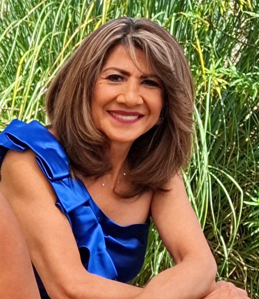 Luz María sonriendo con un vestido azul frente al jardín